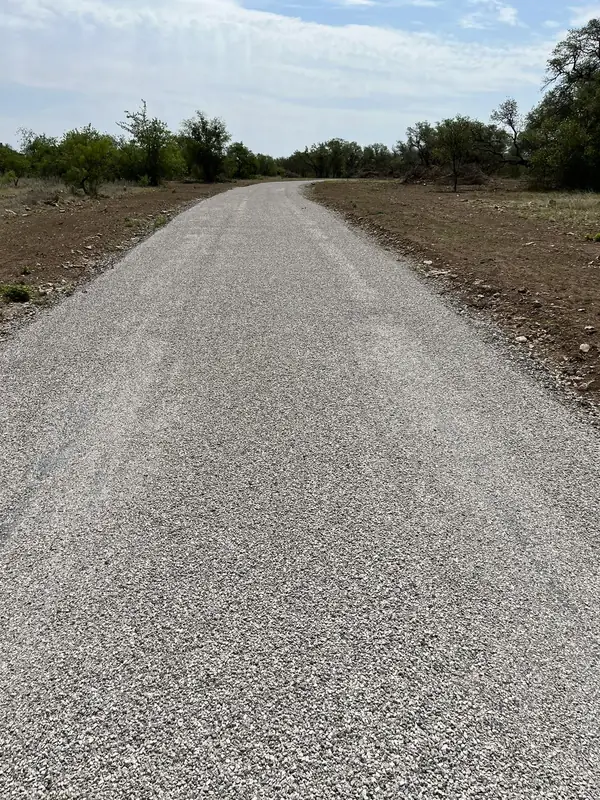 Light gray chip seal road running straight through dry scrub and low brush